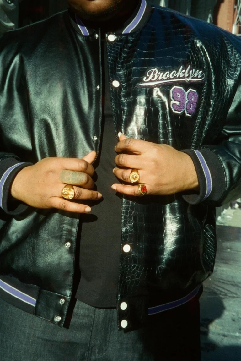 "Close-up of a man wearing a varsity jacket with bold design and gold rings, representing stylish streetwear fashion | Varsity Jacket"